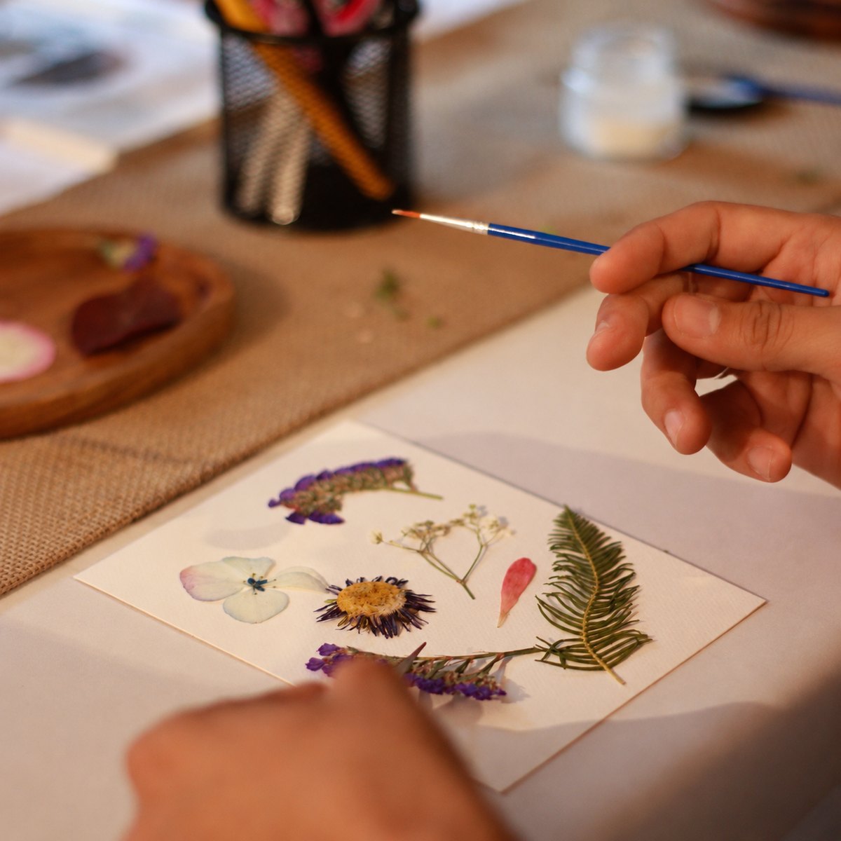 Manos con pincel componiendo flores prensadas sobre papel de algodón
