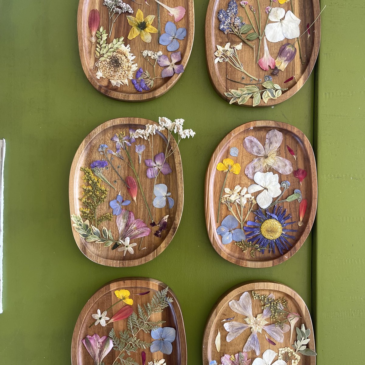 Seis composiciones con flores prensadas sobre bandejas de madera, creadas en el taller