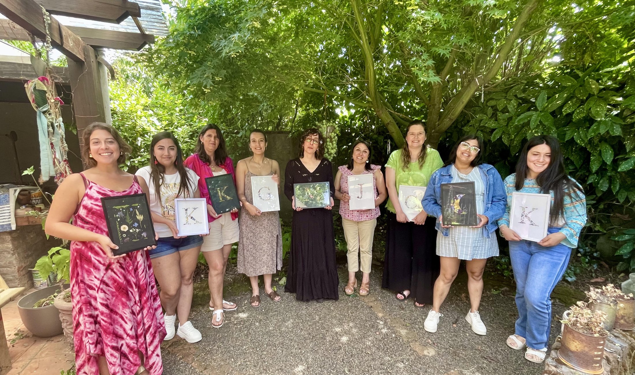 Participantes de un taller de Floriverso en el jardín, mostrando sus cuadros con iniciales de flores prensadas